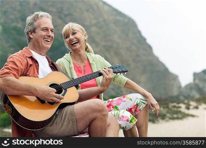 Man Playing Guitar for Woman on Beach