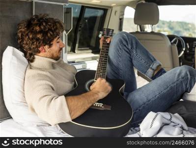 man playing guitar from car while road trip
