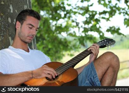 Man playing guitar under tree