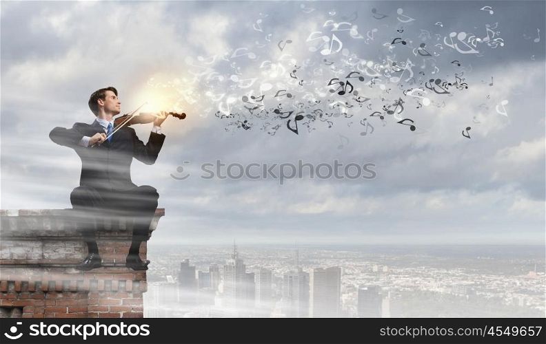 Man playing violin. Young businessman sitting on top of building and playing violin