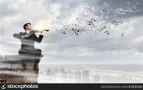 Man playing violin. Young businessman sitting on top of building and playing violin