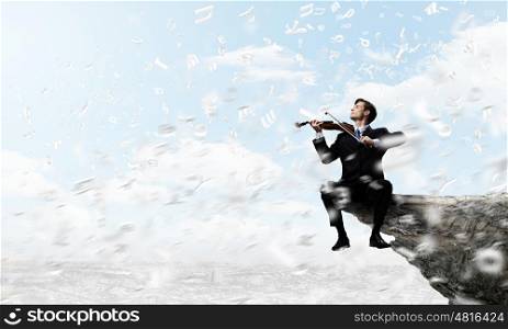 Man playing violin. Young businessman sitting on top of rock and playing violin