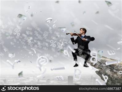 Man playing violin. Young businessman sitting on top of rock and playing violin