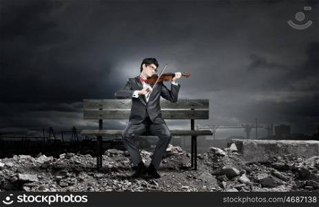 Man playing violin. Young man in suit sitting on bench and playing violin