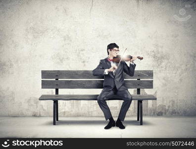 Man playing violin. Young man in suit sitting on bench and playing violin