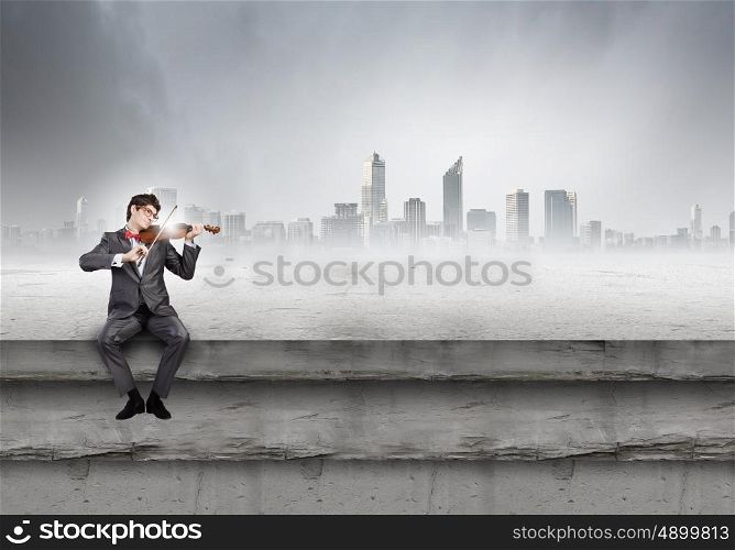 Man playing violin. Young man in suit sitting on building and playing violin
