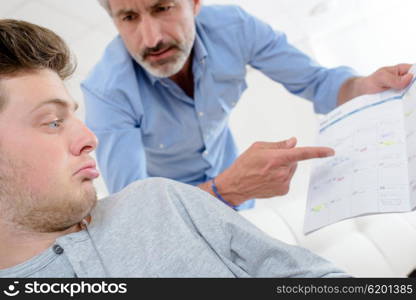 Man pointing angrily at book, young man feigning ignorance