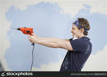 Man pointing drill in front of half painted wall, side view
