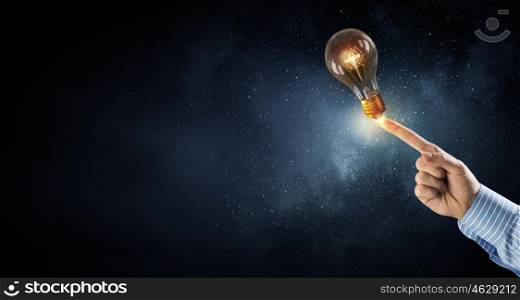 Man pointing light bulb. Businessman pointing with finger on glass glowing light bulb on dark background