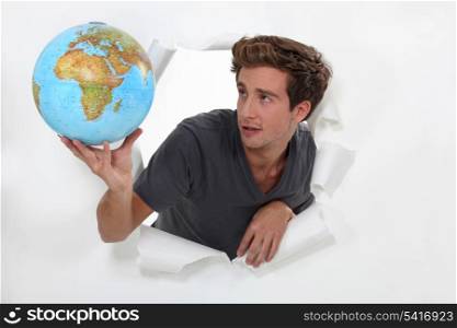 Man popping out a ripped wall in paper holding a globe.