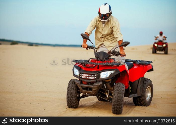 Man poses on atv, downhill riding in desert sands. Male person on quad bike, sandy race, dune safari in hot sunny day, 4x4 extreme adventure, quad-biking. Man poses on atv, downhill riding in desert sands