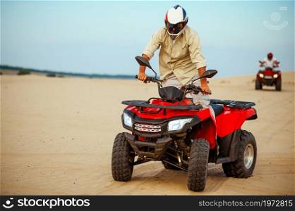Man poses on atv, downhill riding in desert sands. Male person on quad bike, sandy race, dune safari in hot sunny day, 4x4 extreme adventure, quad-biking. Man poses on atv, downhill riding in desert sands