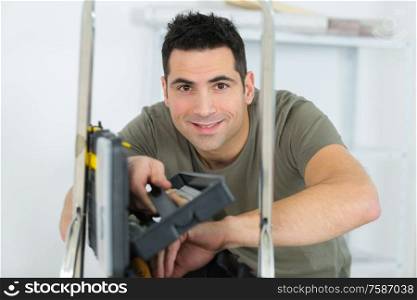 man posing on ladder with toolbox beside him