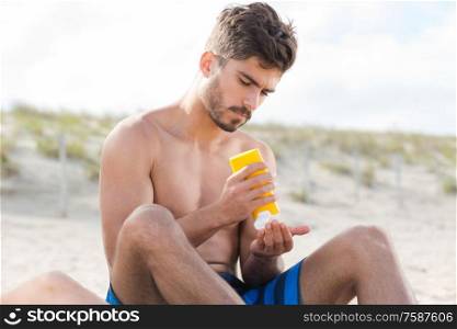 man pouring sunscreen into his hand on the beach