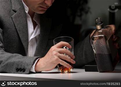 man pours alcohol into a glass in the kitchen after work. Young man suffering from severe headache or migraine sitting with a glass of whiskey in the kitchen. alcohol dependence.. man pours alcohol into a glass in the kitchen after work. Young man suffering from severe headache or migraine sitting with a glass of whiskey in the kitchen. alcohol dependence