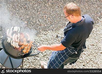 man preparing meat and sausages using a barbecue grill