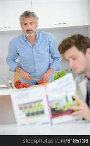 Man preparing vegetables, looking at book held by son
