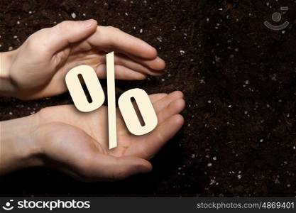 Man presenting his idea. Male hands on soil background showing in palms percent sign