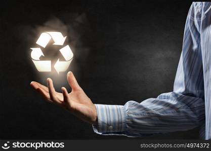 Man presenting recycle symbol. Hand of businessman on dark background holding recycling sign
