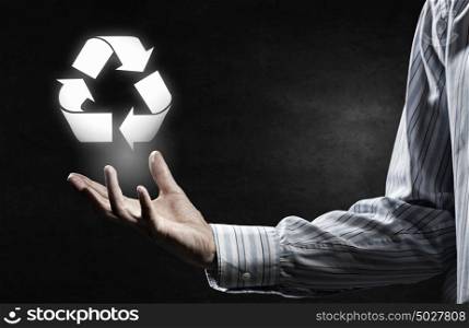 Man presenting recycle symbol. Hand of businessman on dark background holding recycling sign