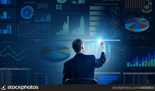 Man presenting report. Rear view of businessman drawing with marker infographs on wall