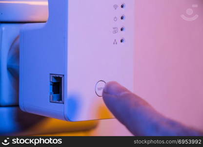 Man press with his finger on WPS button on WiFi repeater which is in electrical socket on the wall. The device help to extend wireless network in home or office.