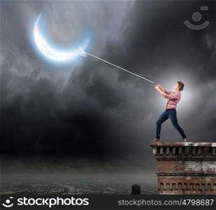 Man pulling moon. Young man in casual catching moon with rope