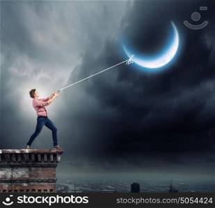 Man pulling moon. Young man in casual catching moon with rope