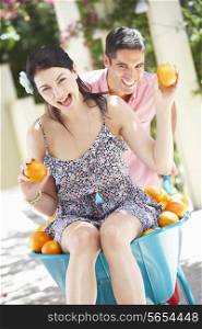 Man Pushing Woman In Wheelbarrow Filled With Oranges