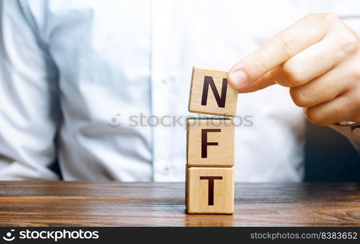 Man puts together word NFT from blocks. NFT non-fungible token. Selling digital art assets through internet auctions. Blockchain technology. Monetization, investment in cryptographic tokens