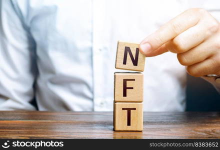 Man puts together word NFT from blocks. NFT non-fungible token. Selling digital art assets through internet auctions. Blockchain technology. Monetization, investment in cryptographic tokens