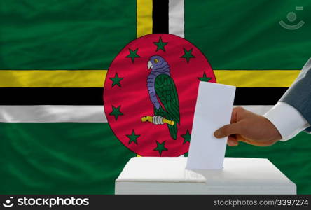 man putting ballot in a box during elections in dominica in fornt of flag