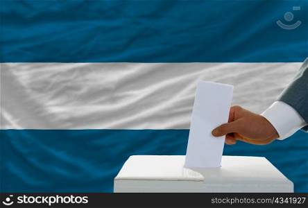 man putting ballot in a box during elections in el salvador in fornt of flag
