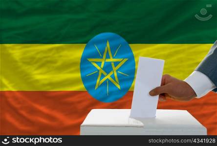 man putting ballot in a box during elections in ethiopia in fornt of flag