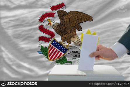 man putting ballot in a box during elections in front of flag american state of illinois
