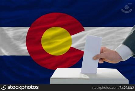 man putting ballot in a box during elections in front of flag american state of colorado