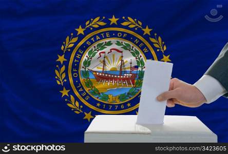 man putting ballot in a box during elections in front of flag american state of new hampshire