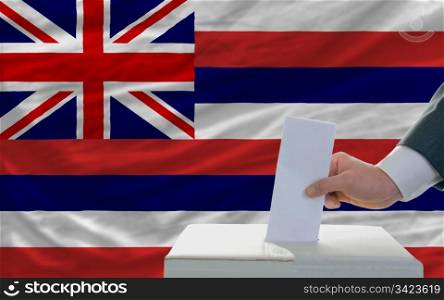 man putting ballot in a box during elections in front of flag american state of hawaii