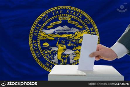 man putting ballot in a box during elections in front of flag american state of nebraska