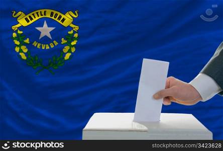 man putting ballot in a box during elections in front of flag american state of nevada