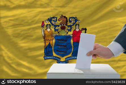 man putting ballot in a box during elections in front of flag american state of new jersey