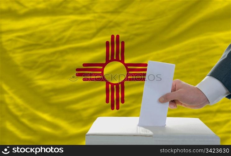 man putting ballot in a box during elections in front of flag american state of new mexico