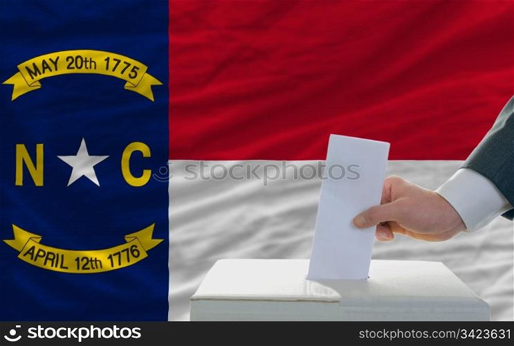 man putting ballot in a box during elections in front of flag american state of north dakota