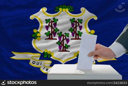 man putting ballot in a box during elections in front of flag american state of connecticut
