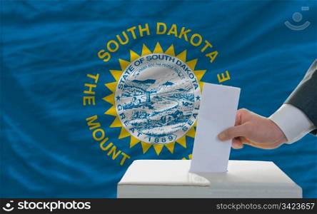 man putting ballot in a box during elections in front of flag american state of south dakota