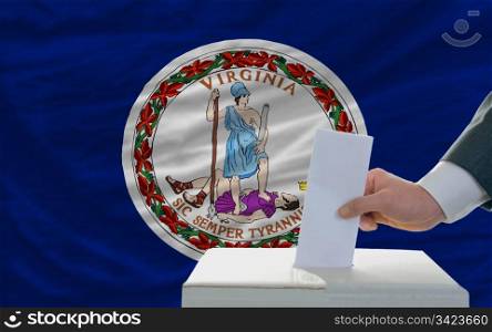 man putting ballot in a box during elections in front of flag american state of virginia