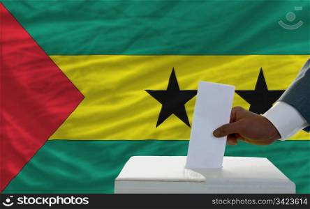 man putting ballot in a box during elections in front of national flag of sao tome principe