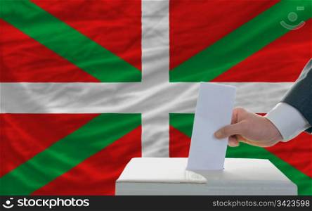 man putting ballot in a box during elections in front of national flag of basque