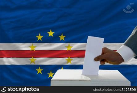 man putting ballot in a box during elections in front of national flag of capeverde