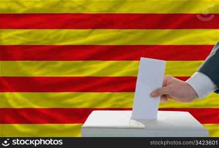 man putting ballot in a box during elections in front of national flag of catalonia